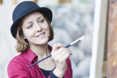 Smiling woman holding brush while painting on canvas