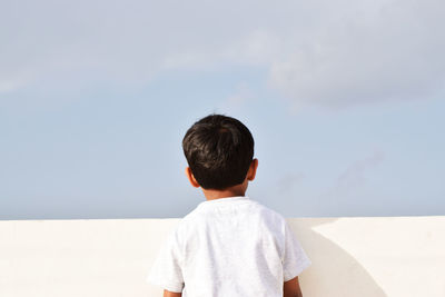 Rear view of boy standing at retaining wall against sky