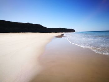 Scenic view of beach against clear blue sky