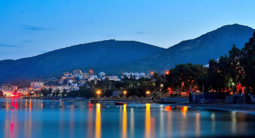 Illuminated city by lake against blue sky at dusk