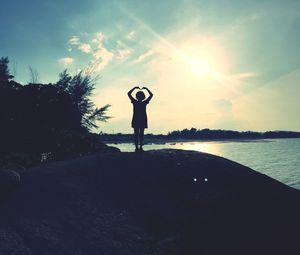 Silhouette man standing at shore against sky during sunset