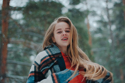 Portrait of young woman standing against trees
