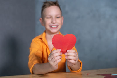 Cute boy cuts out a valentine's day card with hearts. a boy in a bright shirt