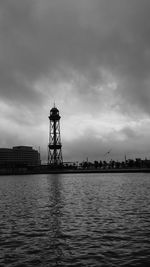 Lighthouse by sea and buildings against sky