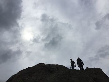 Low angle view of man standing on mountain against cloudy sky