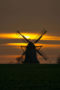 Traditional windmill on field against sky during sunset