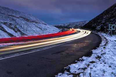 Light trails on road by mountain against sky at night