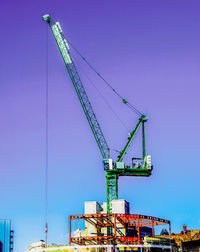 Low angle view of cranes against clear blue sky
