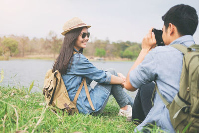 Young man photographing woman with camera while sitting on grassy field