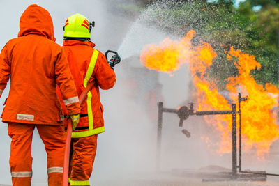 Rear view of firefighter spraying water on fire while standing at street