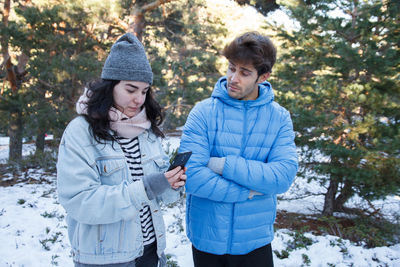 Woman using mobile phone by angry man while standing on snow covered field