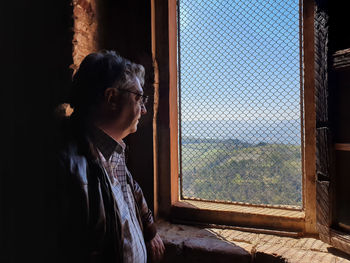 Side view of man looking through window