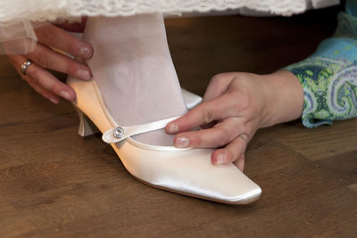 Cropped hands of woman assisting bride wearing shoe on hardwood floor