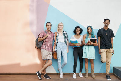 Portrait of happy friends standing against wall