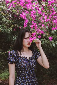 Beautiful young woman standing against pink flowering plants