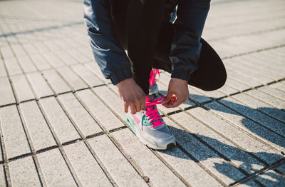 Low section of person tying shoelace while crouching on footpath