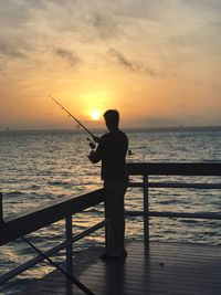 Rear view of silhouette man fishing in sea