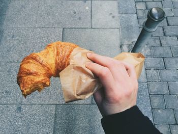 Cropped image of hand holding croissant on footpath