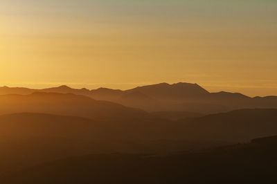 Scenic view of silhouette mountains against orange sky