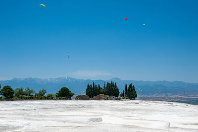 Paragliders flying above white travertines of pamukkale in an ancient city of hierapolis in turkey.