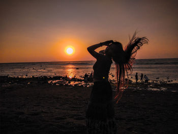 Silhouette woman standing at beach during sunset
