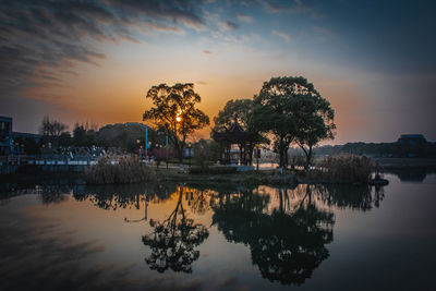 Trees by lake against sky during sunset