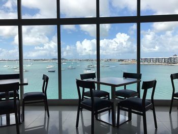 Chairs and table by sea against sky seen through window