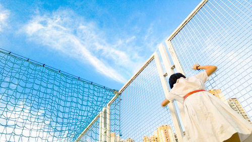 Low angle view of girl standing by fence at schoolyard against sky