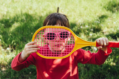 Child girl looking at camera through badminton racket. active lifestyle, outdoor leisure