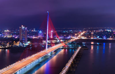 Illuminated bridge over river in city at night