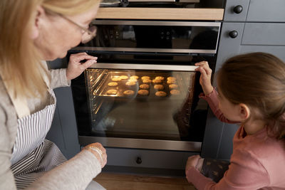 Grandmother and granddaughter looking at cookies in oven