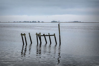 Wooden posts in sea against sky