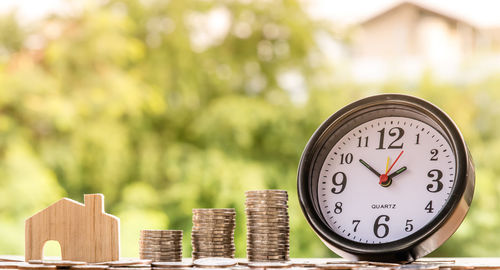 Close-up of clock by coins stacked on table