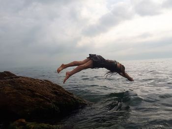 Man jumping on rock in sea against sky