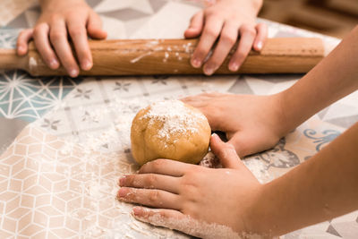 Children's hands prepare to use a rolling pin to roll ginger dough to bake linzer cookies 