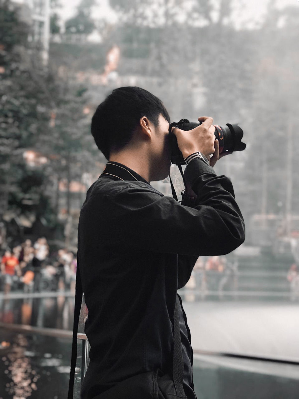 one person, photographing, photography themes, activity, real people, camera - photographic equipment, holding, focus on foreground, waist up, standing, technology, men, leisure activity, photographic equipment, young adult, lifestyles, occupation, young men, city, outdoors, photographer, digital camera, digital single-lens reflex camera