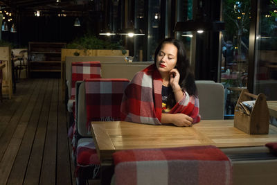 Young woman wrapped in blanket sitting at restaurant