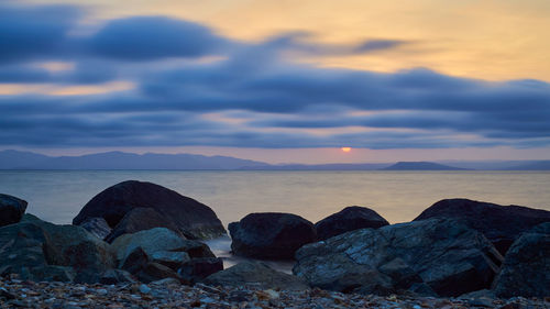 Rocks by sea against sky during sunset