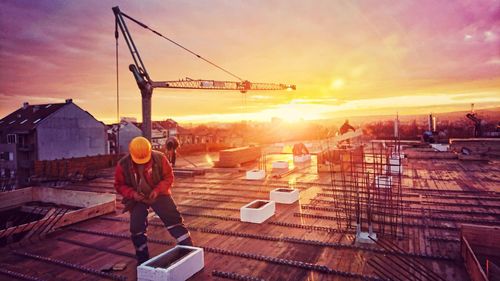 Rear view of man photographing at construction site during sunset