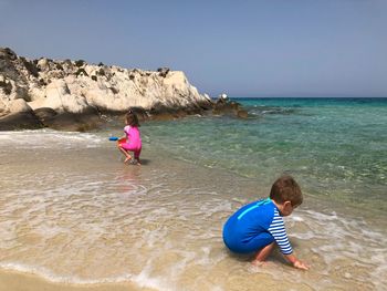 Siblings playing on beach against sky