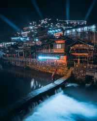 Man standing by illuminated buildings against sky at night