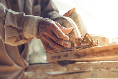 Midsection of carpenter using circular saw on wood