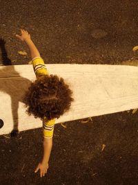 Directly above of child standing with arms outstretched on road