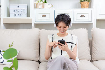 Young woman using mobile phone while sitting on bed at home