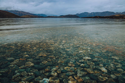 Scenic view of stony shore and lake against sky