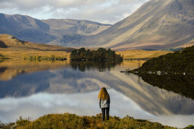 Rear view of man looking at lake against mountain range