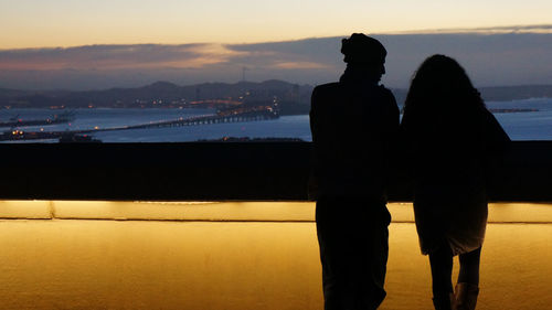 Silhouette couple standing by sea against sky during sunset