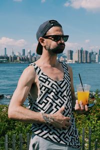 Man drinking juice while standing against sea and sky in city