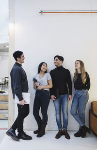 Full length of happy entrepreneurs talking while standing against white wall in office