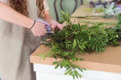 Midsection of florist cutting leaf stems at table